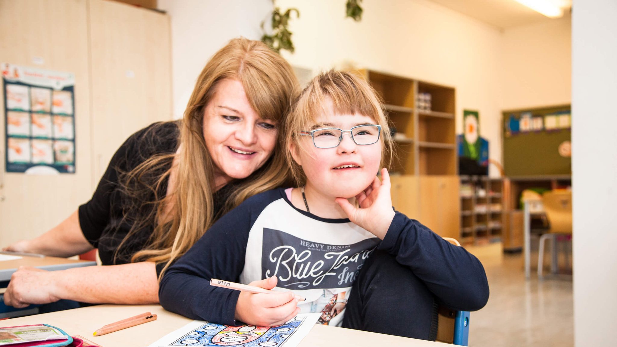 Kind mit Beeinträchtigung sitzt mit Schulassistenz in Klassenzimmer